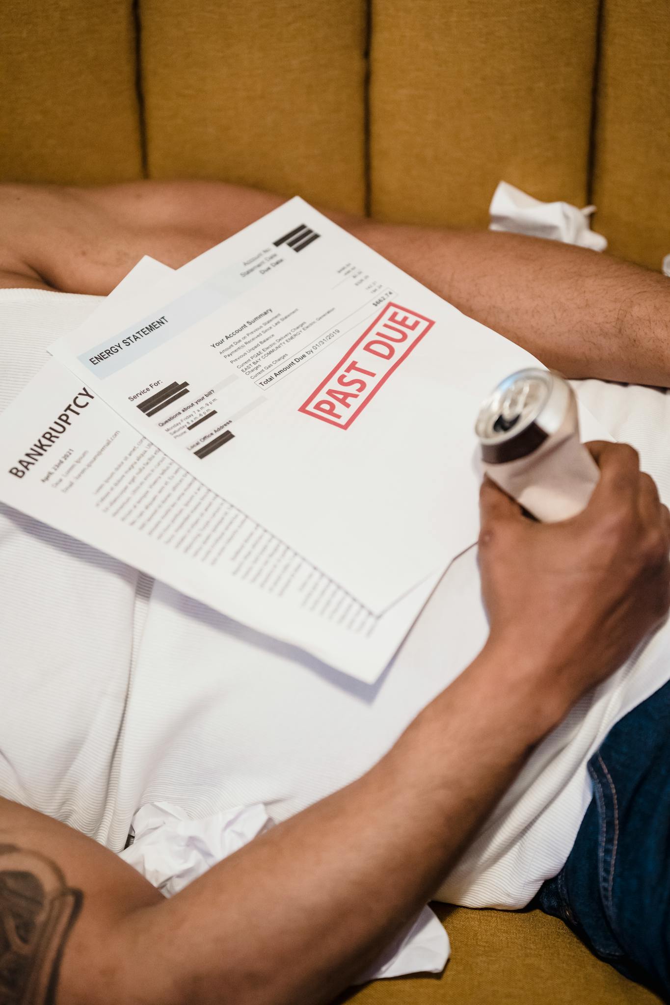 An adult male holding a can of beer with visible bankruptcy and past due notices.